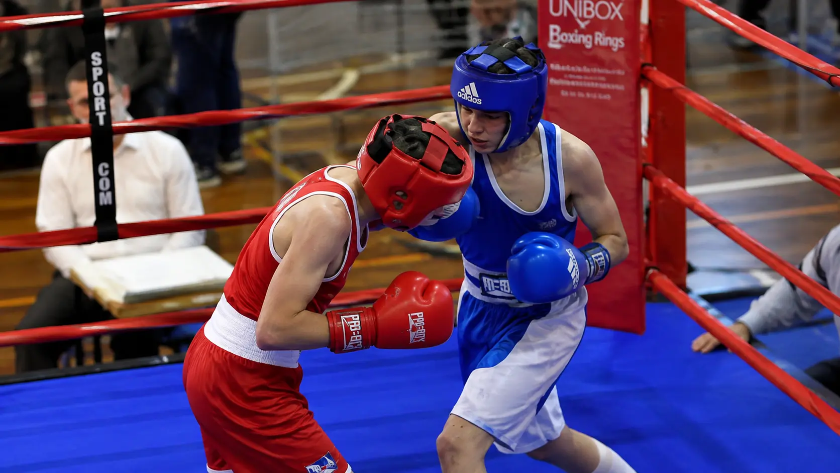 Two amateur boxers, red corner and blue corner, exchanging punches in the ring